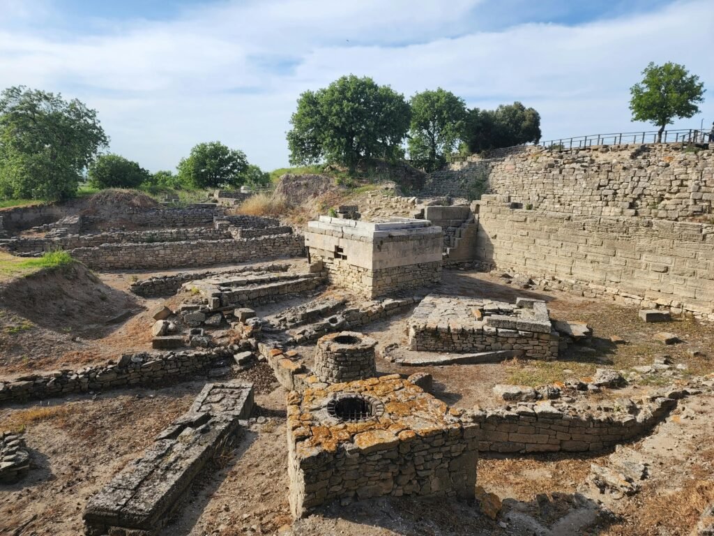 pexels-photo-12646211-12646211 Explore the ancient ruins of Troy in Çanakkale, Turkey, showcasing historical stone structures under a cloudy sky.
